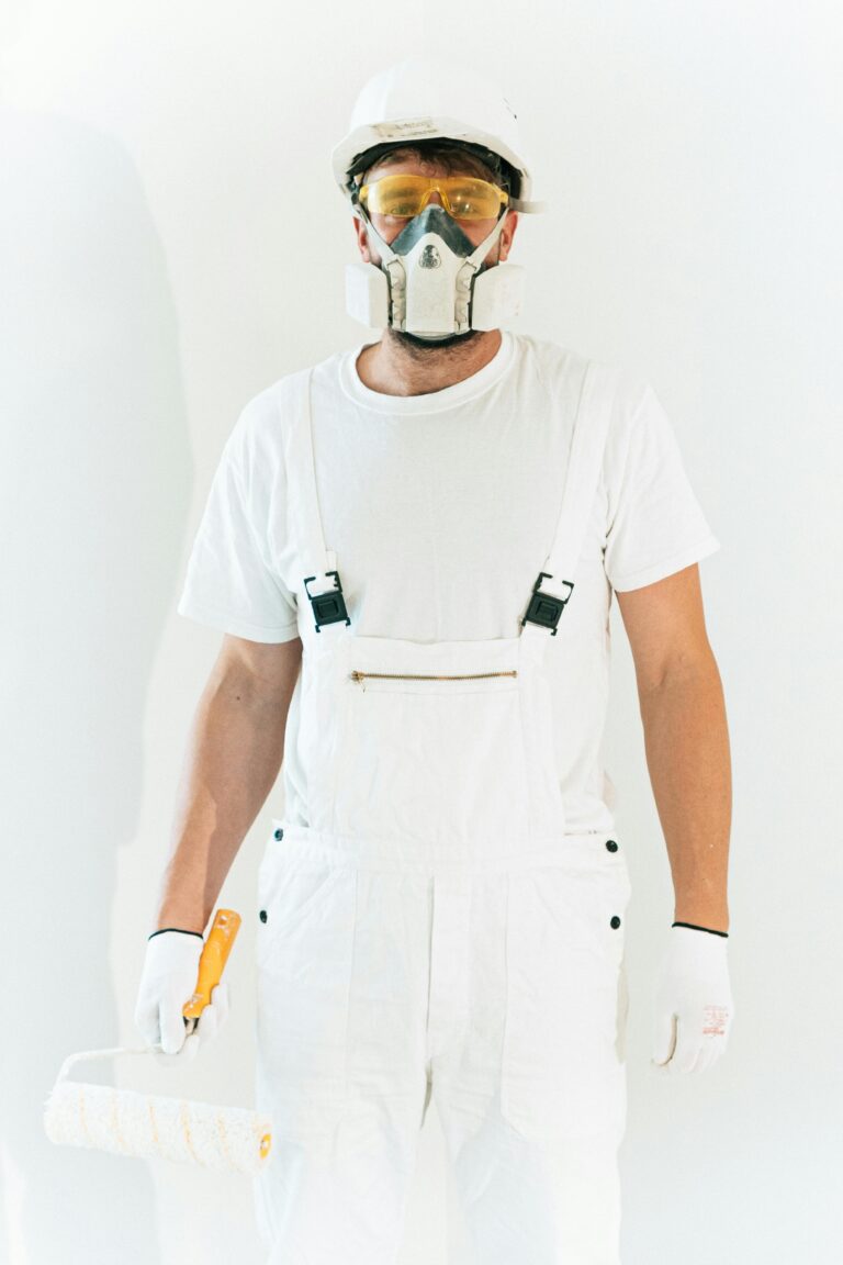 Man wearing safety gear holding a paint roller in a bright setting, showcasing professional painting attire.