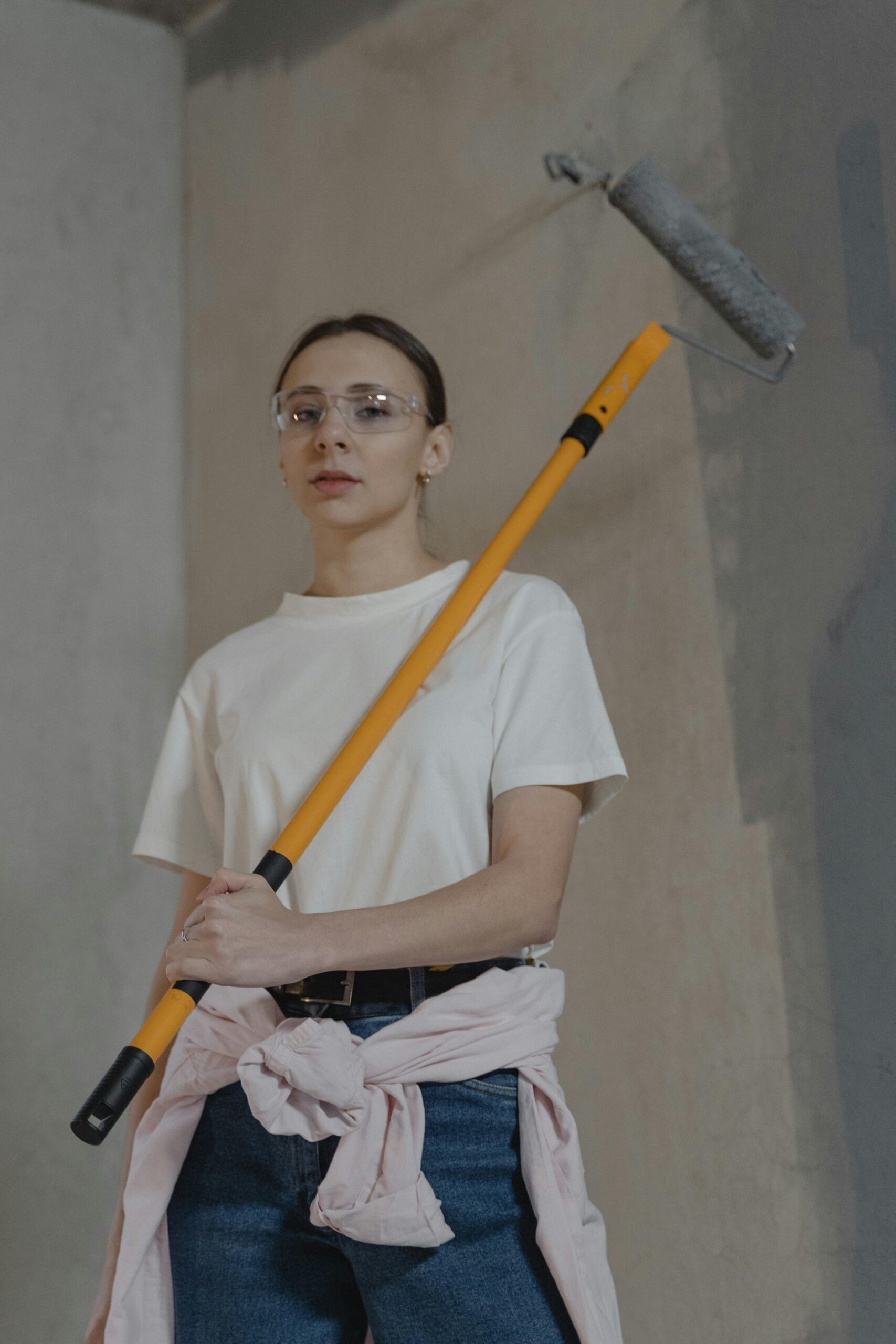 Female painter renovating a wall indoors with a paint roller, wearing safety goggles.